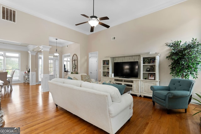 living room featuring ceiling fan, decorative columns, a towering ceiling, wood-type flooring, and ornamental molding