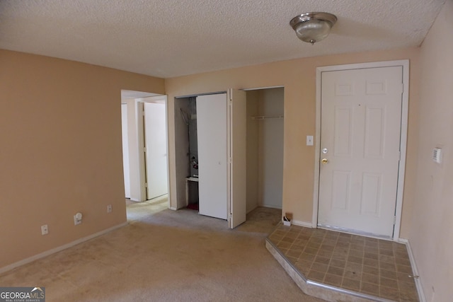 interior space featuring a textured ceiling, light colored carpet, and multiple closets