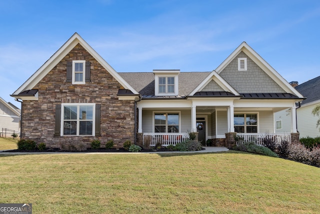 craftsman-style home featuring roof with shingles, a standing seam roof, stone siding, covered porch, and a front yard