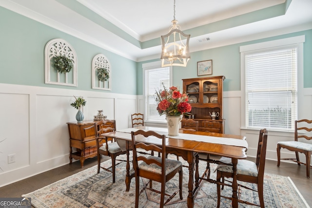 dining room with a raised ceiling, a decorative wall, a notable chandelier, and wainscoting