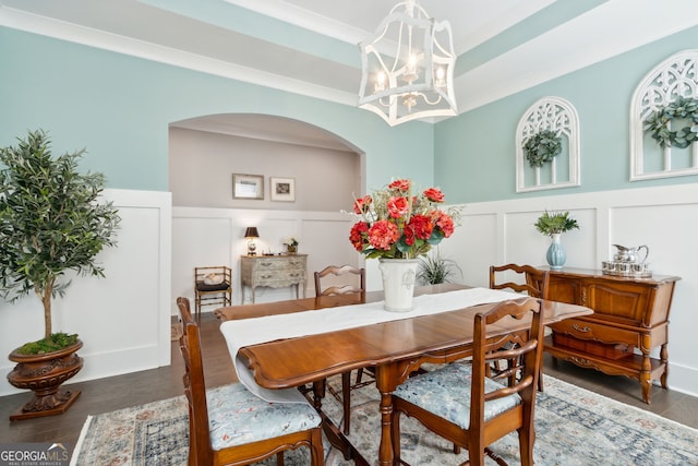 dining area with a wainscoted wall, arched walkways, an inviting chandelier, wood finished floors, and a decorative wall