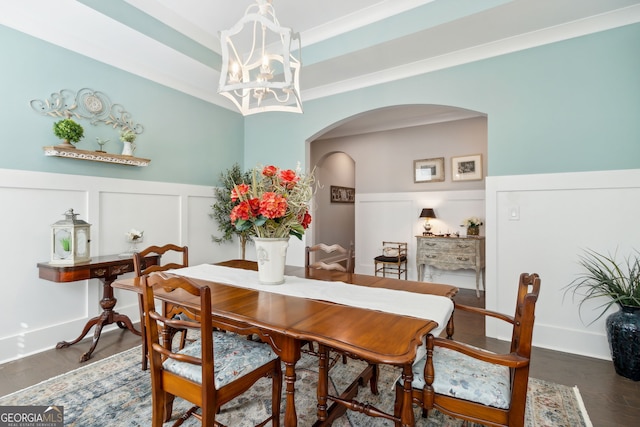 dining room with a decorative wall, wood finished floors, wainscoting, a chandelier, and arched walkways