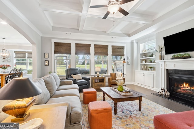 living room featuring hardwood / wood-style floors, ornamental molding, beamed ceiling, ceiling fan with notable chandelier, and coffered ceiling