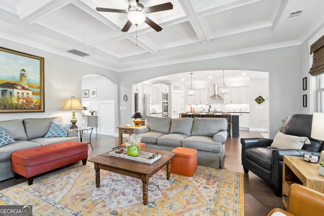 living room with coffered ceiling, hardwood / wood-style flooring, beamed ceiling, crown molding, and ceiling fan