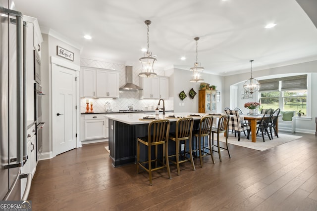 kitchen with wall chimney exhaust hood, white cabinets, decorative light fixtures, and dark wood-type flooring