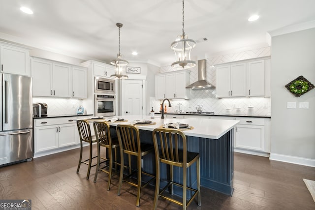 kitchen featuring dark wood-type flooring, appliances with stainless steel finishes, wall chimney range hood, and pendant lighting