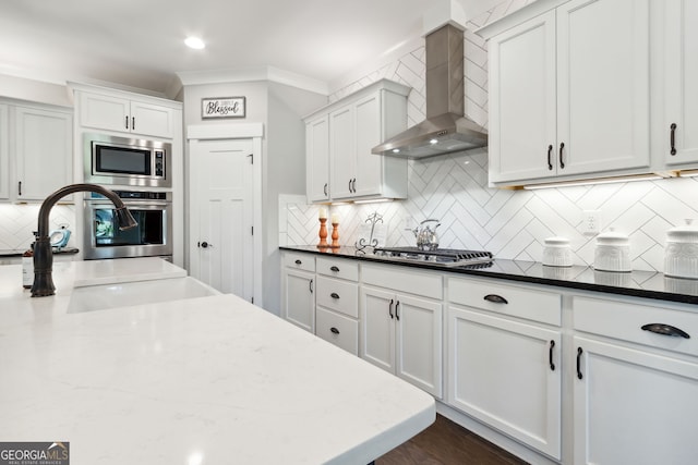 kitchen featuring wall chimney exhaust hood, appliances with stainless steel finishes, white cabinets, and tasteful backsplash