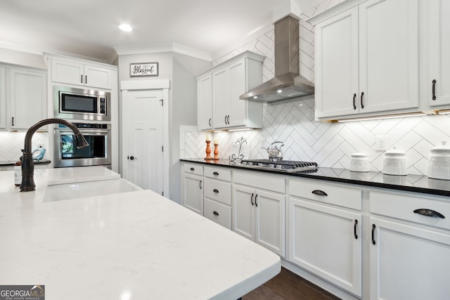 kitchen featuring white cabinets, stainless steel appliances, wall chimney range hood, a sink, and tasteful backsplash