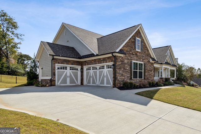 view of property exterior with fence, a yard, driveway, stone siding, and roof with shingles
