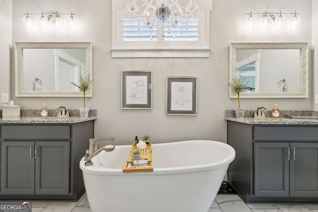 bathroom with marble finish floor, a notable chandelier, a freestanding tub, and two vanities