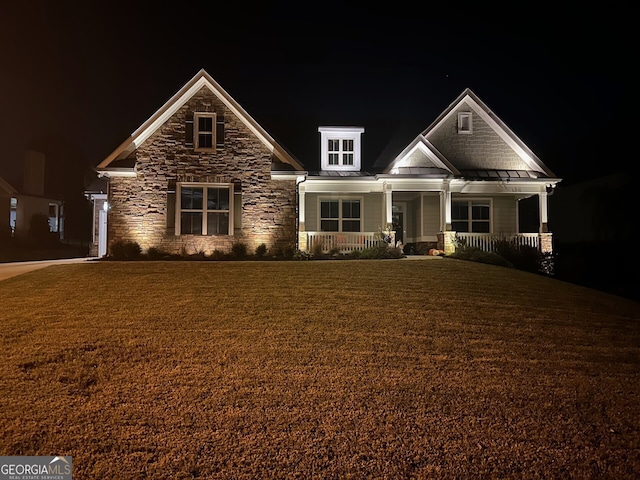 craftsman-style house with a yard, a standing seam roof, stone siding, a porch, and metal roof