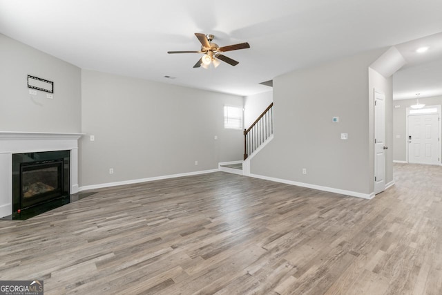 unfurnished living room with light wood-style floors, baseboards, stairway, and a fireplace with flush hearth