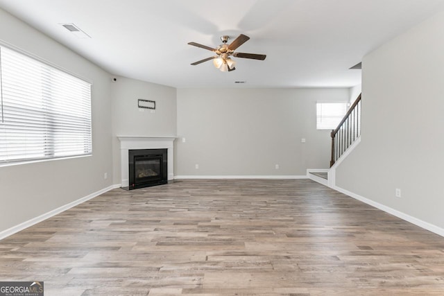 unfurnished living room with a fireplace with flush hearth, light wood-style floors, stairway, and baseboards