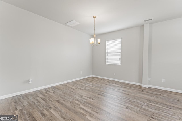 empty room featuring a notable chandelier and light wood-type flooring