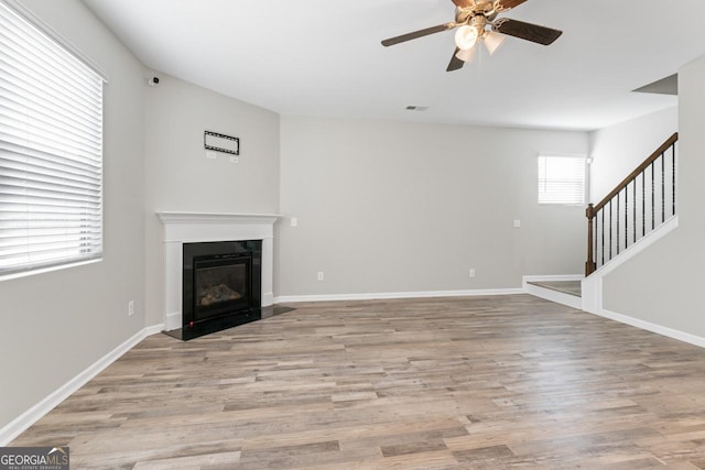 unfurnished living room featuring visible vents, baseboards, a glass covered fireplace, stairway, and light wood-style floors