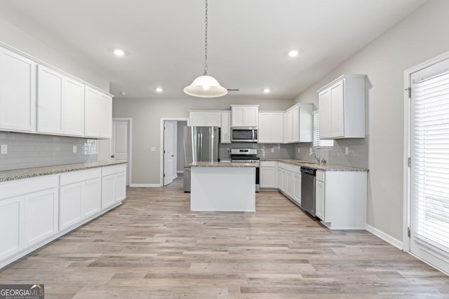 kitchen with appliances with stainless steel finishes, a kitchen island, white cabinetry, and light stone countertops