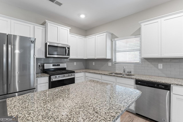 kitchen with light stone counters, visible vents, appliances with stainless steel finishes, white cabinetry, and a sink