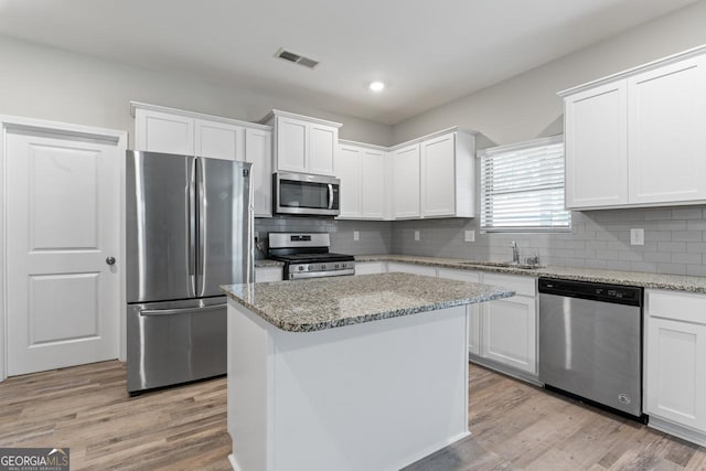 kitchen featuring sink, white cabinetry, light stone counters, appliances with stainless steel finishes, and a kitchen island