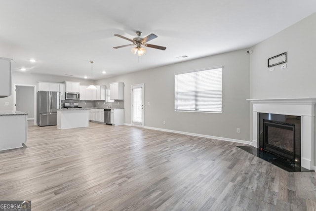 unfurnished living room featuring ceiling fan, light wood finished floors, a fireplace with flush hearth, and baseboards