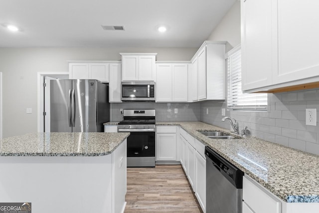 kitchen with sink, white cabinets, a center island, stainless steel appliances, and light stone countertops