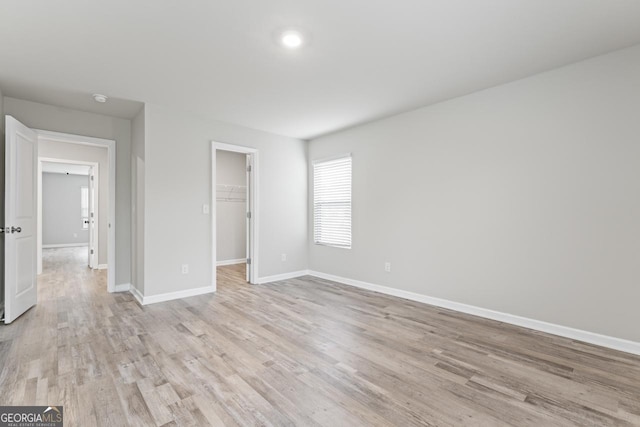 unfurnished bedroom with light wood-style flooring, baseboards, a walk in closet, and a closet