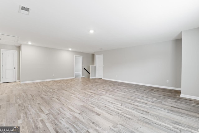 unfurnished living room featuring visible vents, baseboards, attic access, and light wood-style floors