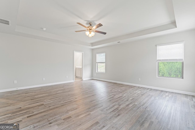 spare room featuring light wood-style flooring, baseboards, a raised ceiling, and a ceiling fan