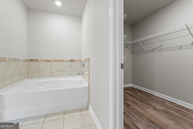 full bathroom featuring tile patterned flooring, a spacious closet, baseboards, and a bath