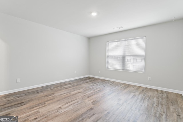 empty room featuring light wood-type flooring, visible vents, and baseboards