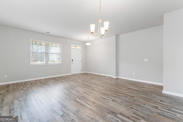 unfurnished room with baseboards, wood finished floors, visible vents, and a notable chandelier