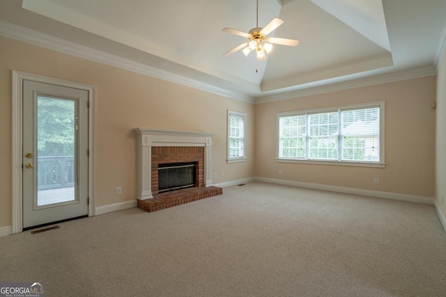 unfurnished living room with a tray ceiling, a brick fireplace, ceiling fan, light carpet, and ornamental molding