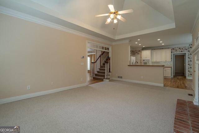 unfurnished living room with ornamental molding, light carpet, a tray ceiling, and ceiling fan