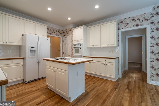 kitchen with a kitchen island, white cabinetry, light wood-type flooring, crown molding, and white appliances