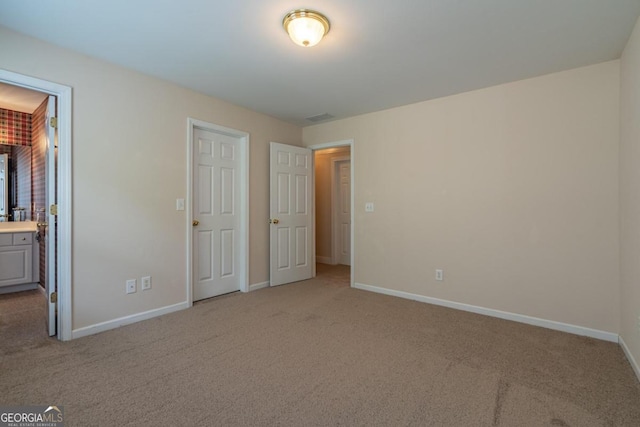 unfurnished bedroom featuring light carpet and ensuite bathroom