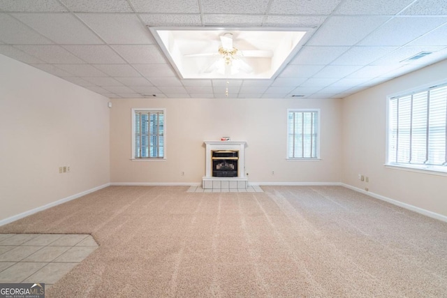 unfurnished living room featuring a tiled fireplace, ceiling fan, carpet flooring, and a paneled ceiling