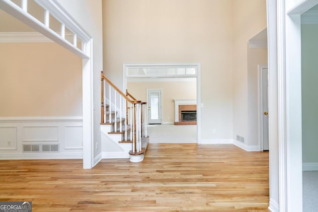 entryway featuring a towering ceiling, ornamental molding, a brick fireplace, and light wood-type flooring