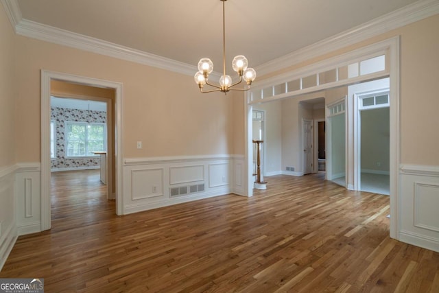 unfurnished dining area featuring crown molding, hardwood / wood-style floors, and a notable chandelier