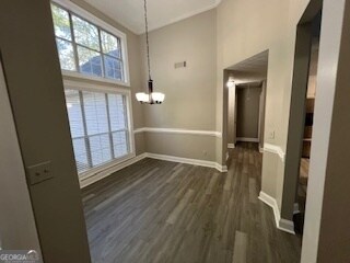 unfurnished dining area with a high ceiling, an inviting chandelier, and dark hardwood / wood-style flooring