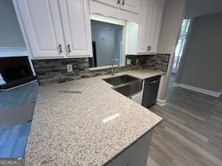 kitchen with decorative backsplash, hardwood / wood-style flooring, sink, white cabinets, and light stone counters