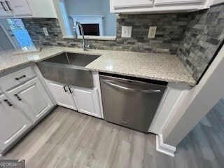 kitchen with sink, stainless steel dishwasher, white cabinets, light stone counters, and light hardwood / wood-style flooring