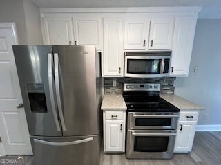 kitchen with light stone countertops, appliances with stainless steel finishes, white cabinets, decorative backsplash, and light hardwood / wood-style flooring