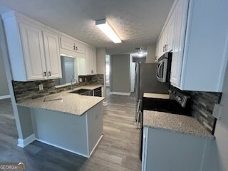 kitchen with appliances with stainless steel finishes, light stone countertops, light wood-type flooring, kitchen peninsula, and white cabinetry