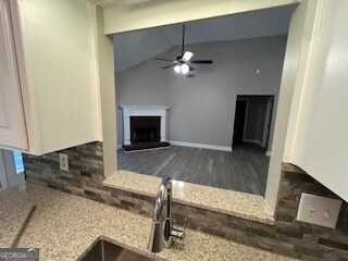 kitchen with lofted ceiling, hardwood / wood-style flooring, light stone counters, and ceiling fan