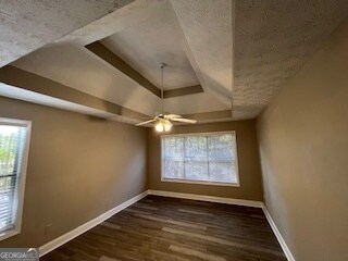 empty room with ceiling fan, a tray ceiling, and dark hardwood / wood-style floors