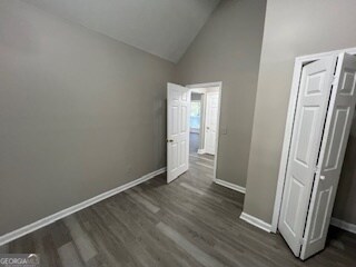 unfurnished bedroom featuring a closet, dark wood-type flooring, and high vaulted ceiling