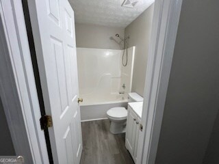 full bathroom with  shower combination, a textured ceiling, toilet, vanity, and hardwood / wood-style flooring