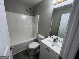 full bathroom featuring toilet, tub / shower combination, wood-type flooring, vanity, and a textured ceiling