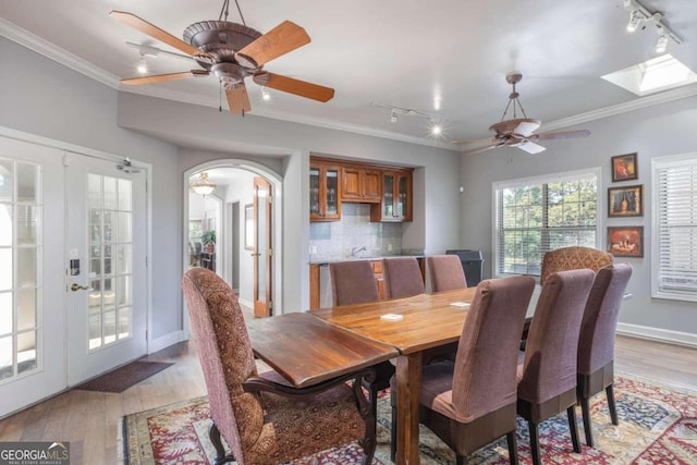 dining space with french doors, rail lighting, crown molding, and light hardwood / wood-style floors