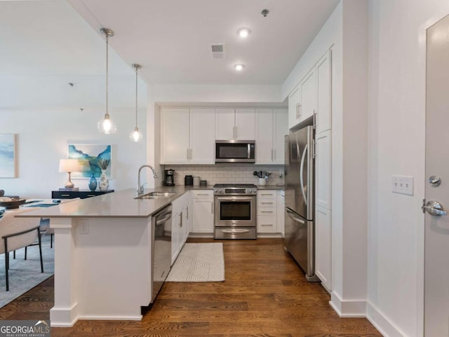 kitchen featuring dark hardwood / wood-style floors, kitchen peninsula, stainless steel appliances, sink, and decorative light fixtures