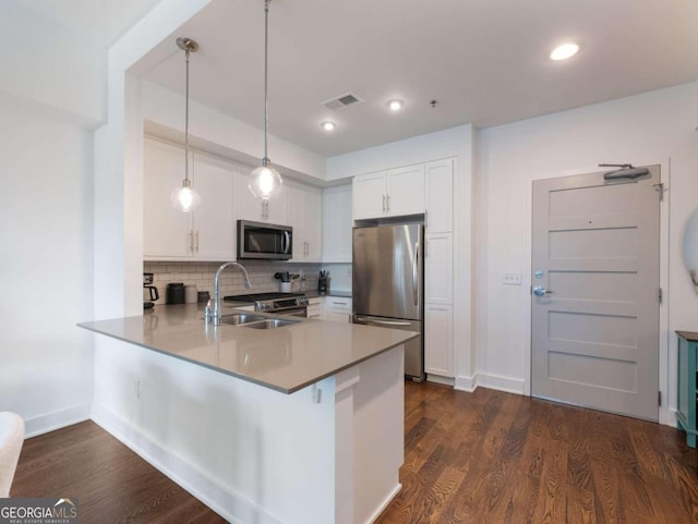 kitchen featuring hanging light fixtures, kitchen peninsula, white cabinetry, appliances with stainless steel finishes, and dark hardwood / wood-style flooring